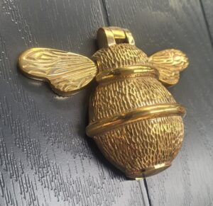 Polished brass bee door knocker mounted on a dark textured composite door.